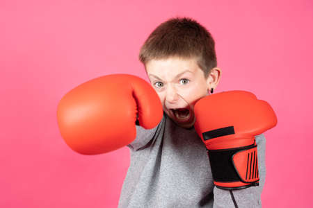 Aggressive teenager boy giving a punch and looking at camera isolated on pink background. Bullying defense concept.の写真素材