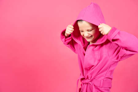 Cheerful cute little girl wearing housecoat isolated on vivid pink background.の写真素材
