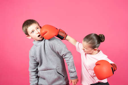 Little girl wearing boxing gloves hitting bully boy isolated on pink background. Woman power and...