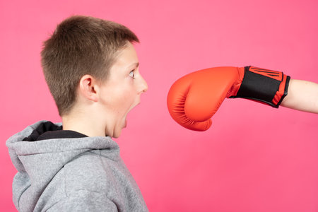 Surprised boy with fear receiving a punch of hand wearing boxing glove. Bullying revenge and self...