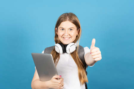 Pretty college student making ok sign and holding laptop isolated on blue background. Back to school concept.の写真素材