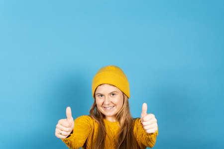 Positive pretty young woman smiling to camera with thumbs up isolated on blue background with copy...
