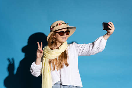 Young pretty tourist woman taking selfie isolated on blue background.
