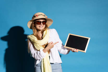 Scandinavian tourist woman wearing straw hat and pointing at blackboard isolated on blue background.の写真素材