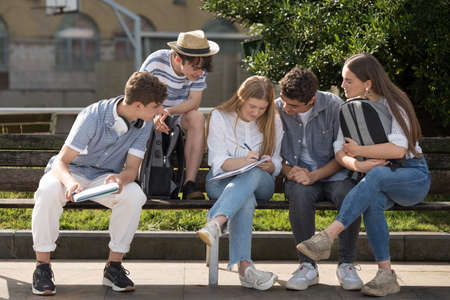 College students working and learning together in a park. Teenager friends sitting on a bench.の写真素材