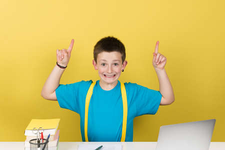 Cute schoolboy pointing up to copy space isolated on yellow background. Back to school concept