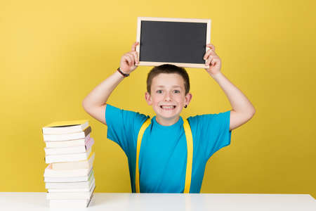 Student boy raising blackboard with copy space over the head isolated on yellow background.
