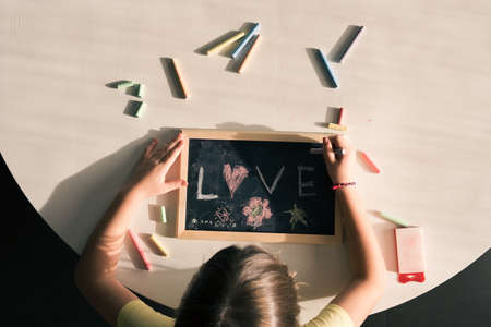 View from above of child drawing and writing love with chalk on blackboard.の写真素材
