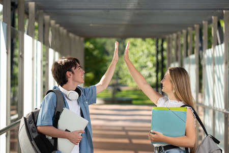 Student boy and girl high five each other in a college corridorの写真素材