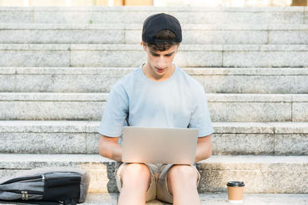 Handsome student boy sitting on stairs and working on laptopl