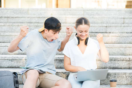 Teenager boy and girl celebrating good news. Students using laptop.の写真素材