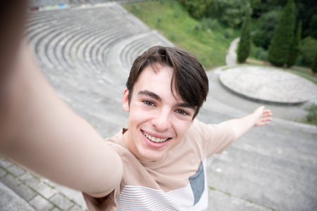 Young teenager tourist boy taking a selfie in touristic destination. Happy adolescent looking and smiling at camera in amphitheaterの写真素材
