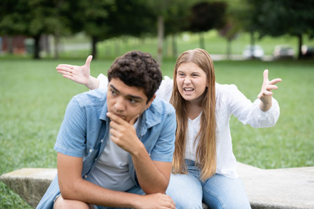 Toxic girl shouting and threatening boyfriend. Hispanic boy ignoring girlfriend outdoors in a parkの写真素材