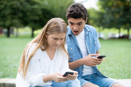 Surprised teenager boy spying phone to girlfriend outdoors in a park.の写真素材