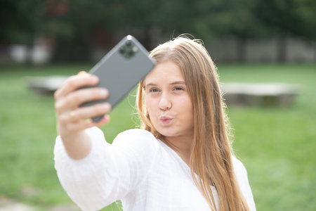 Teenager girl taking selfie and doing kissing gesture while looking at phone.の写真素材