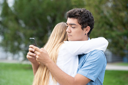 Hispanic teenager boy hugging girlfriend and chatting on phone. Cheating and infidelity conceptの写真素材