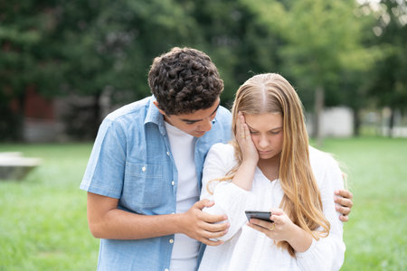 Teenager girl receiving bad news on phone and boyfriend supporting and hugging her. Anxiety and social media concept.の写真素材