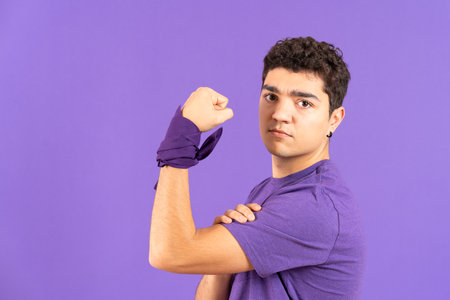 Feminist hispanic boy showing strength and holding biceps isolated on purple backgroundの写真素材