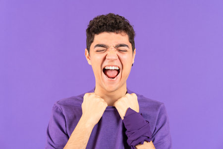 Despaired hispanic teenager boy shouting out loud isolated on purple background.の写真素材