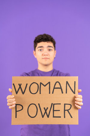 Hispanic boy holding cardboard billboard isolated on purple background. Feminism and woman power...