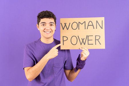 Hispanic teenager boy pointing at billboard isolated on purple background. Feminism and woman power concept.の写真素材