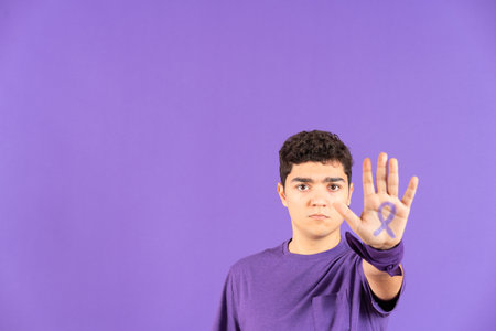 Hispanic teenager boy showing purple ribbon drawn on hand isolated on purple background with copy space. Feminism, woman rights and equality concept.の写真素材