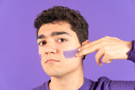 Feminist activist hispanic boy painting face isolated on purple background. Feminism and equality conceptの写真素材