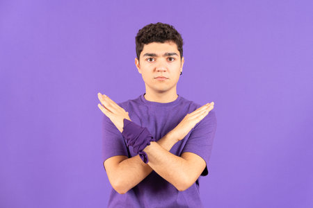 Hispanic teenager boy saying no with hands isolated on purple background. Feminism and gender violence conceptの写真素材