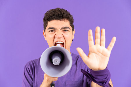 Angry protestor man shouting on megaphone and making stop gesture with hand isolated on purple background. Feminism and equality conceptの写真素材
