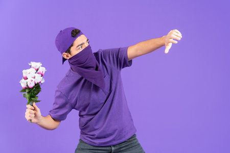 Young male unrecognizable protestor throwing flowers to enemy isolated on purple background. Feminism and equality concept. Man fighting for woman rightsの写真素材