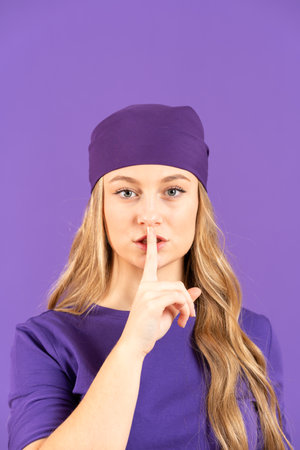 Young pretty woman making silence gesture finger on lips isolated on purple background. Feminism, gender violence and equality conceptの写真素材