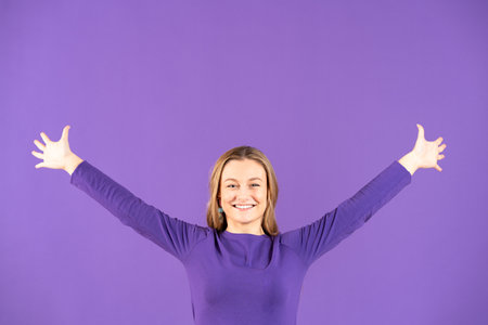 Pretty young woman outstretching arms and feeling free smiling at camera isolated on purple backgroundの写真素材