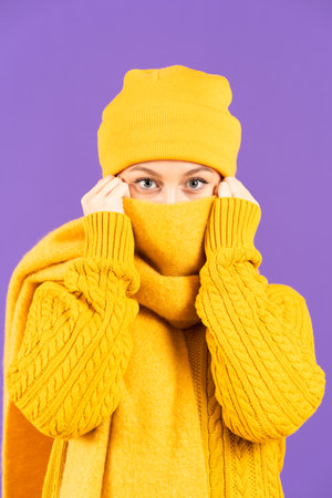 Winter clothing unrecognizable woman covering face with scarf while looking at camera isolated on purple backgroundの写真素材