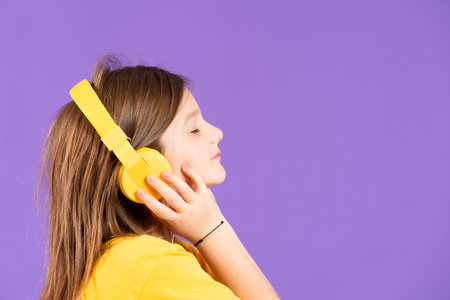 Side view of cute little girl listening to music on headphones isolated on purple background with...