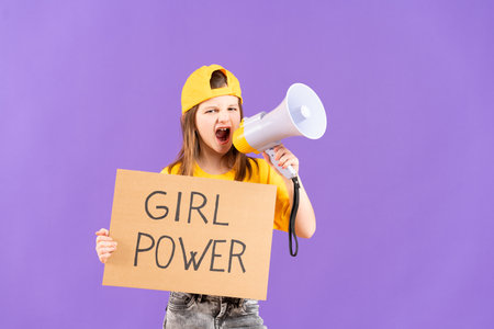 Cute protestor kid shouting on megaphone and showing girl power message on cardboard isolated on purple backgroundの写真素材