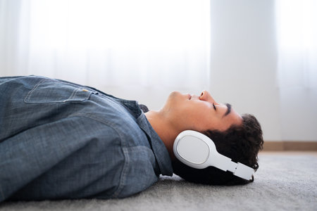 Side view of hispanic teenager boy listening to relaxing music on headphones and relaxing with closed eyesの写真素材