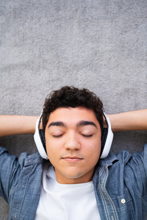 Hispanic teenager boy listening to relaxing music while lying on carpet with copy space.の写真素材