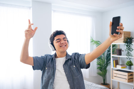 Hispanic teenager boy listening to music on headphones, dancing and singing in the living roomの写真素材