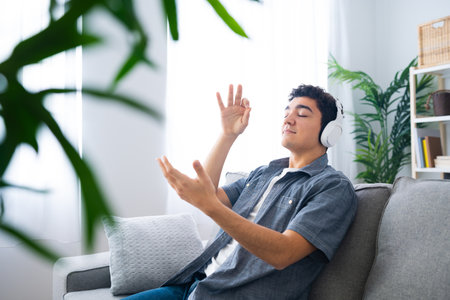 Hispanic teenager boy listening to relaxing music on headphones and enjoying the moment in the living roomの写真素材