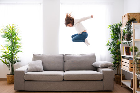 Little girl jumping on sofa in the living room. Kid playing at home. hyperactivity conceptの写真素材