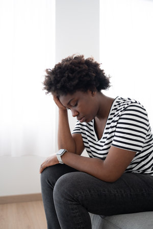 Sad black woman sitting on couch hand on head. Depression, anxiety, racism and bullying concept.の写真素材