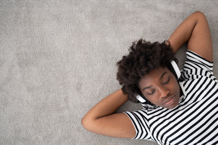 Relaxing African American listening to music on headphones and dreaming with copy space. Young black woman lying on carpetの写真素材
