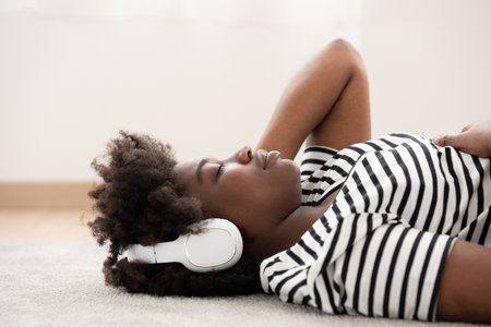 African American woman listening to music on headphones while lying on the floor.の写真素材