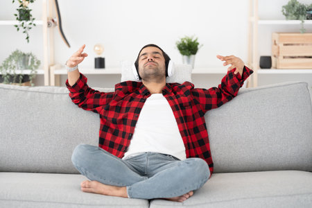 Hispanic young man listening relaxing music indoors, sitting on sofa.の写真素材