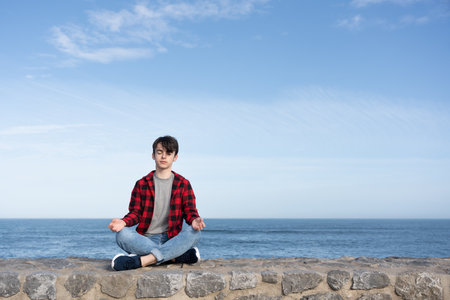 Teenager boy meditating outdoors at the coast. Introspection and mental health conceptの写真素材