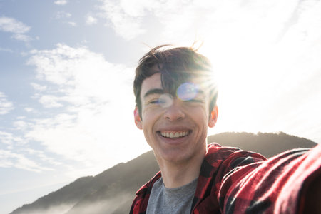 Selfie portrait of smiling cheerful teenager boy outdoors with lens flare.の写真素材