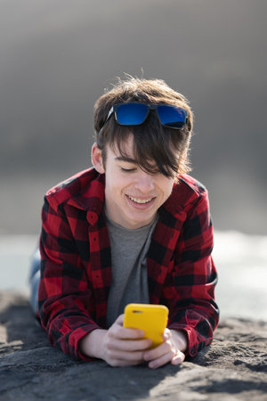 Teenager boy chatting on phone outdoors. Smiling person using telephone.の写真素材