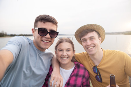 Group of teenagers taking selfie outdoors beside lake.