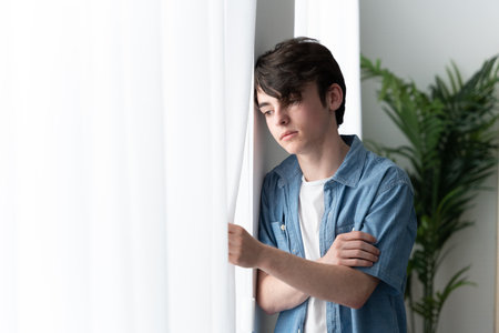Sad teenager boy looking through window. Depression, sadness and anxiety concept