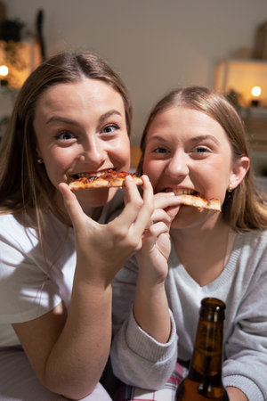 Sisters having fun while eating pizza and looking at camera at home.の写真素材